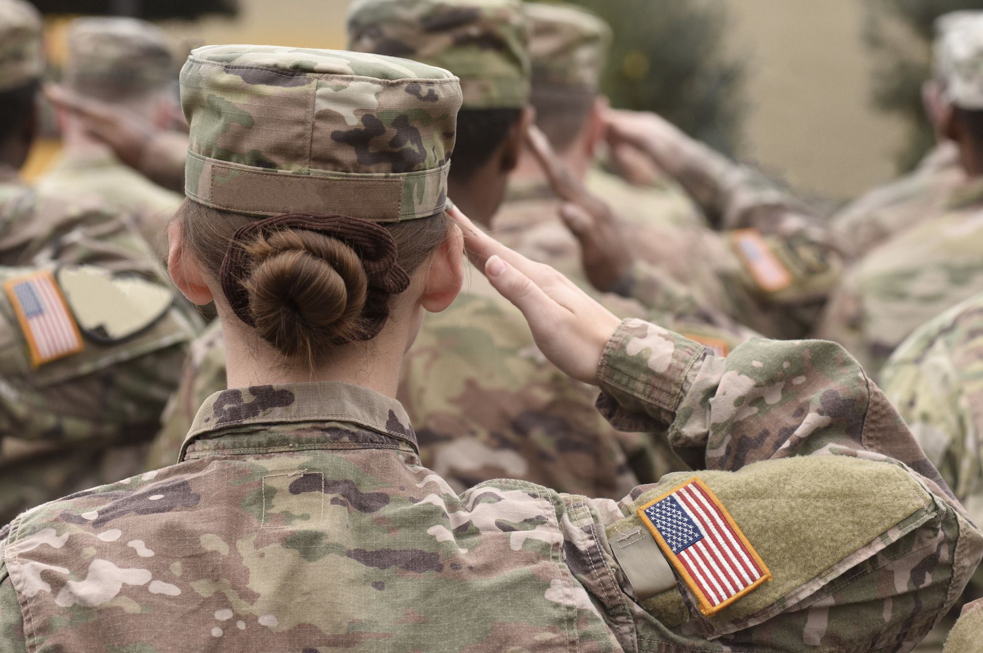 Soldiers in camouflage uniforms saluting during a military ceremony outdoors