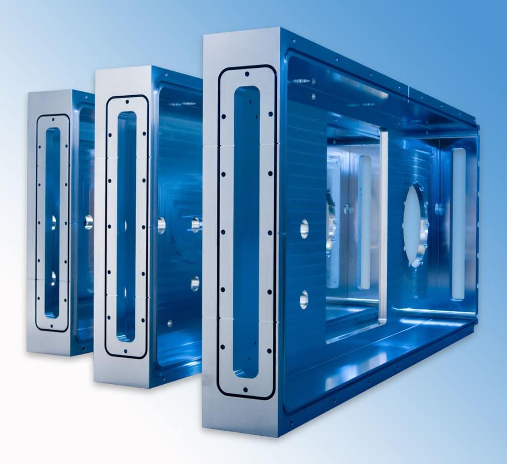 Three large rectangular hog-out aluminum deposition chambers with multiple ports, used for solar panel manufacturing.