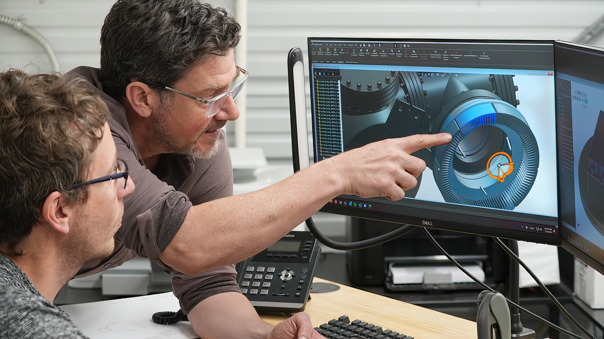 Two engineers are looking at a computer screen together showing a solid model of a vacuum chamber.
