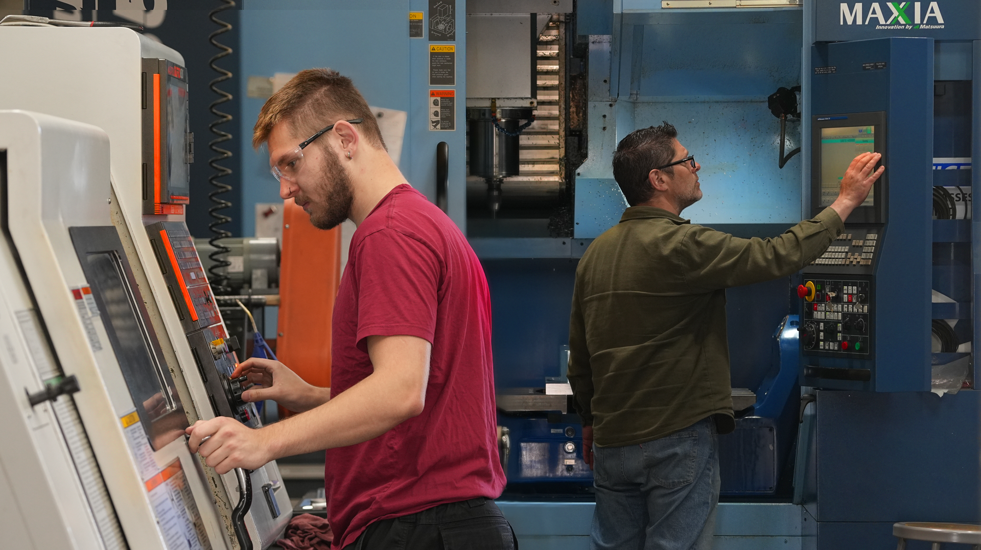 Two machinists in the Atlas factory, one operating a Mazak lather and the other a 5 axis Matsuura CNC mill.