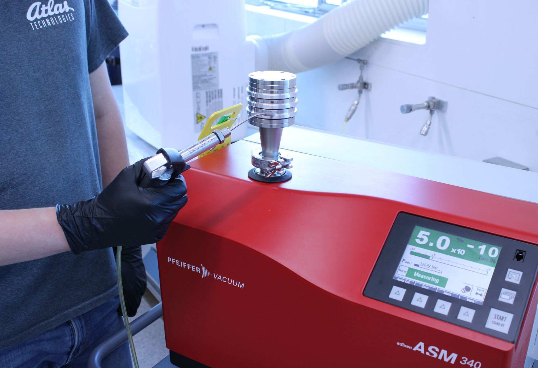 A man helium leak testing a bimetal flange using an ASM 340 leak tester for UHV applications. 