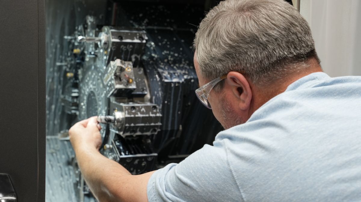 A man is adjusting the spindle on a cutting machine in a factory.