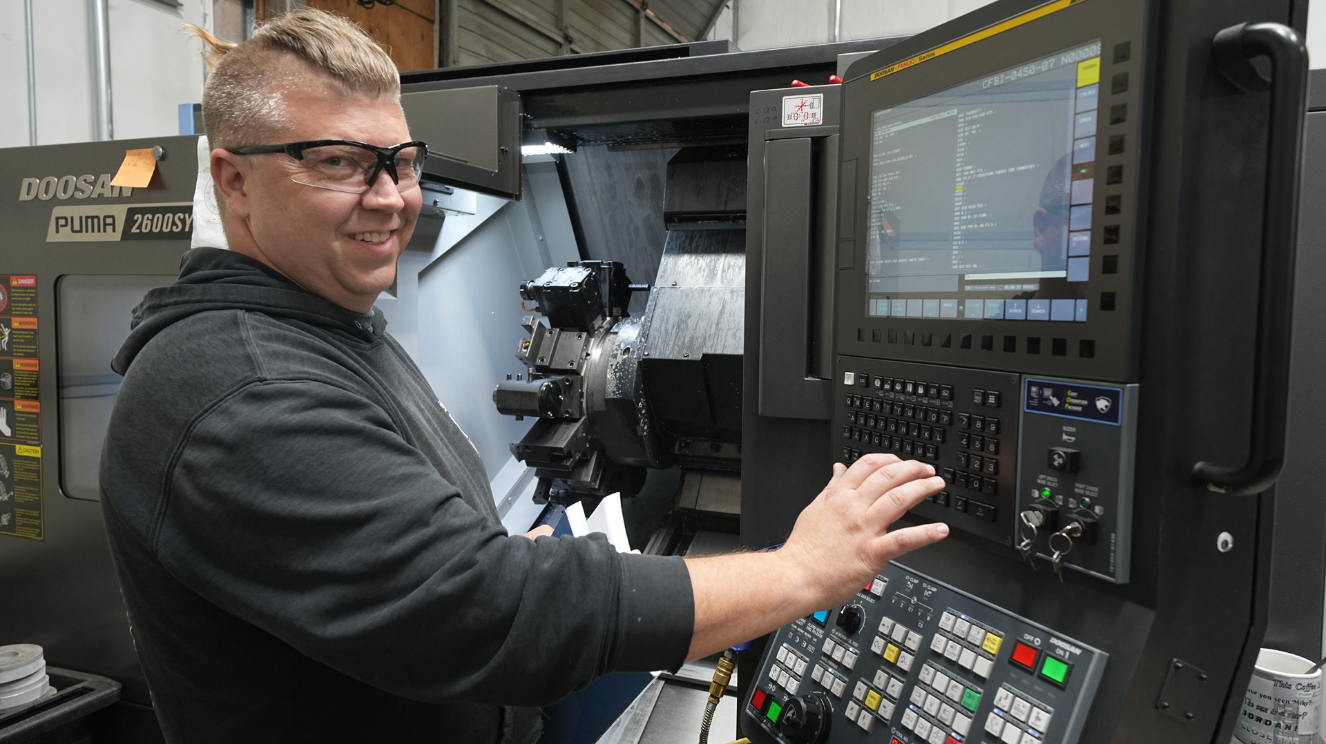 A man with safety glasses operates a cutting machine in a factory.