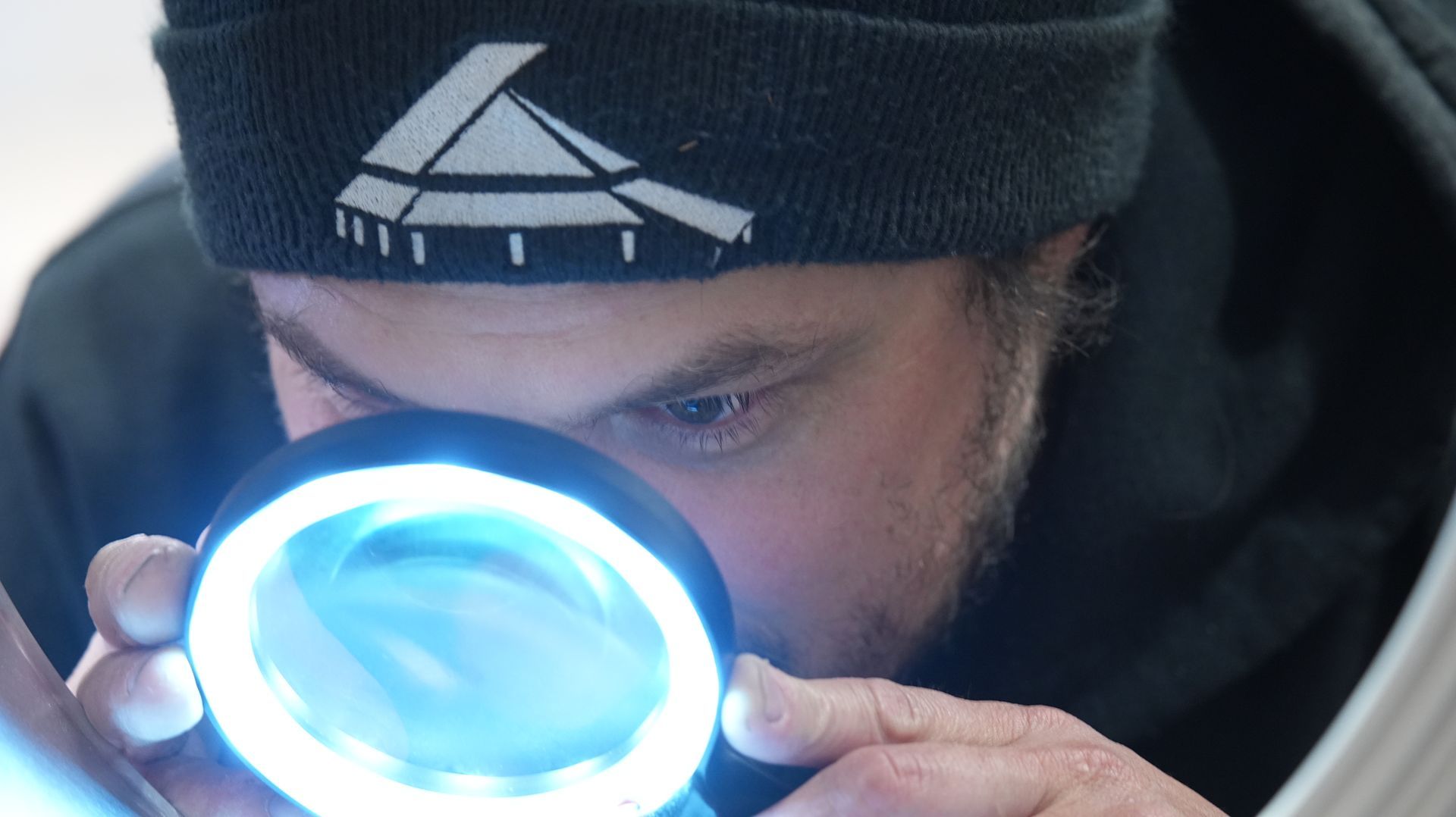 A man is looking through a magnifying glass to inspect a bonded and welded component. 