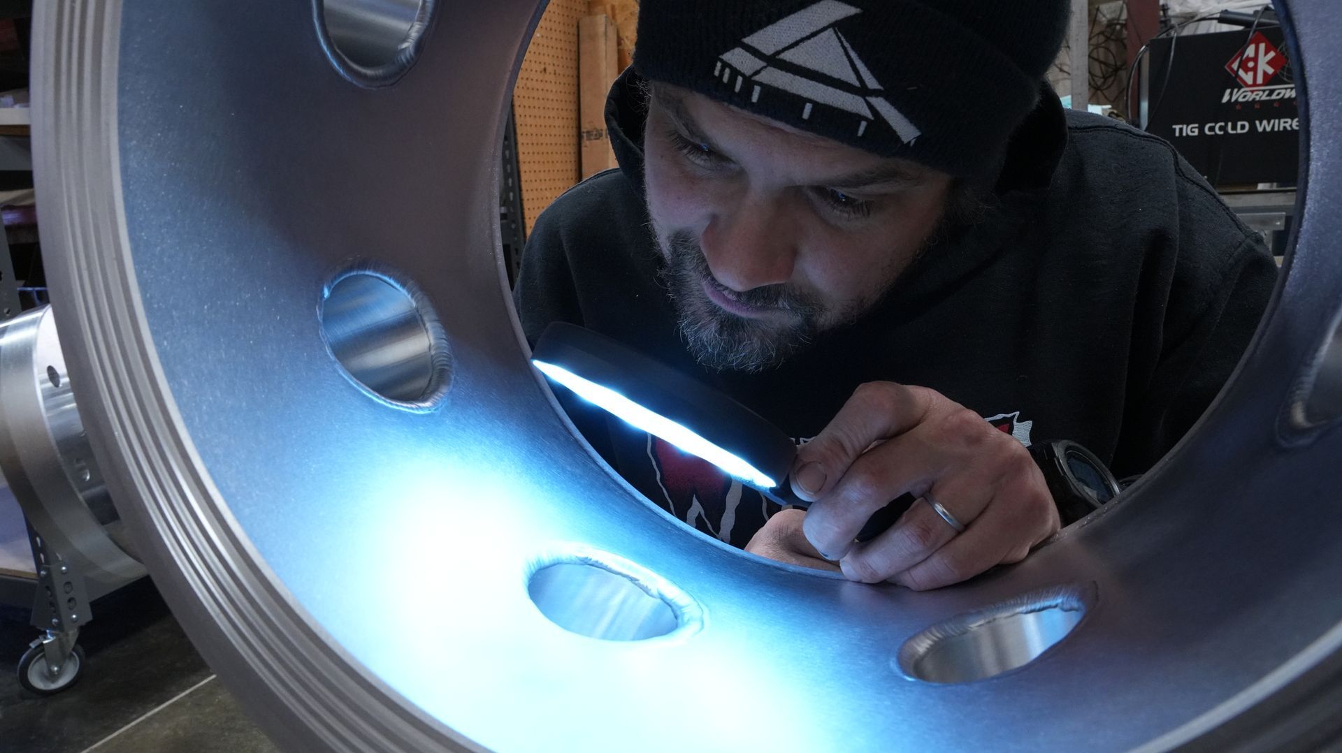 A man uses a magnifying glass to inspect the weld on a large aluminum chamber 