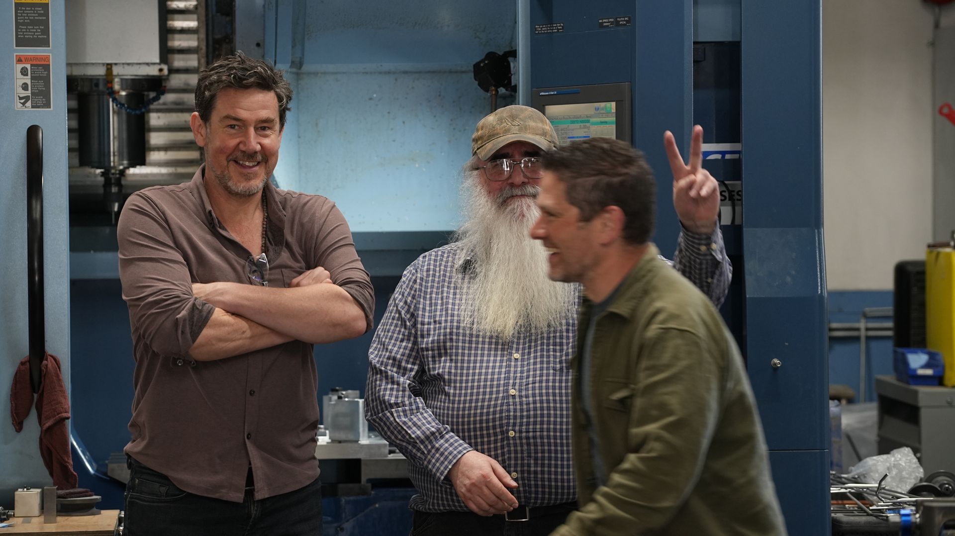 Three laughing men are standing next to each other in a factory.