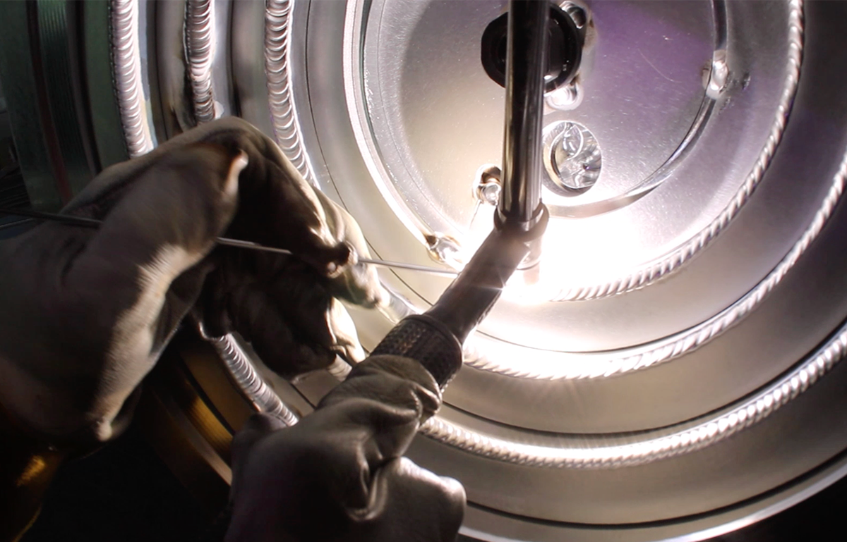 A close up of a person TIG welding water cooling channels used in the lid of an aluminum vacuum chamber.