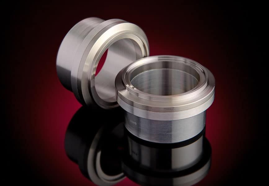 Two bimetal aluminum-stainless tube transition couplings on reflective red background.