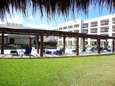 A large building with a swimming pool and chairs under a thatched roof.