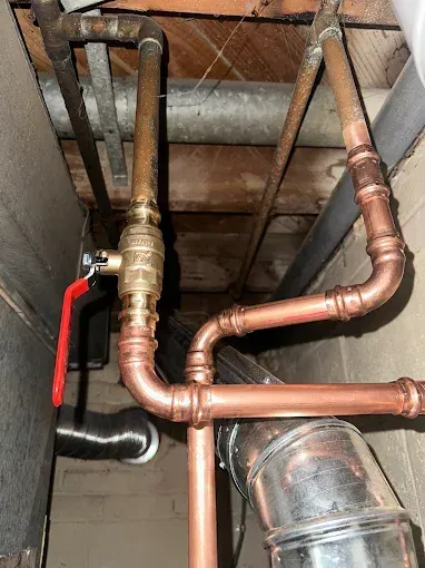 Copper pipes and ball valve in a basement, with a red handle.