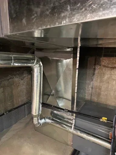 Metal HVAC ductwork with a furnace in a basement setting.