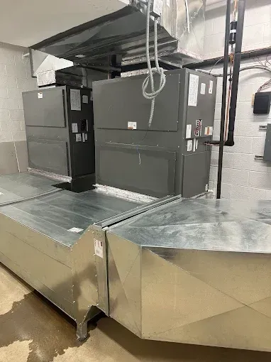 HVAC units with silver ducts against a light wall in a utility room.