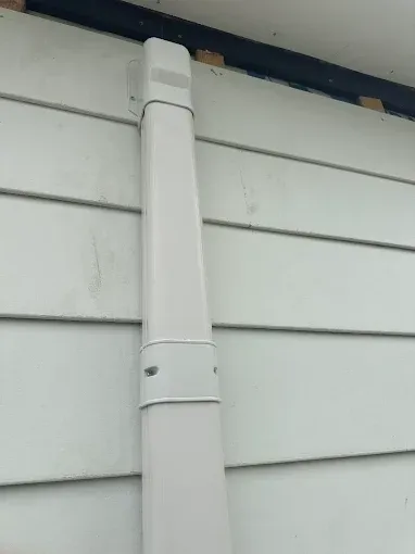 White rectangular downspout on a white clapboard siding of a building.