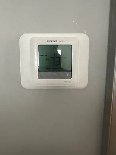 White Honeywell thermostat on a gray wall; the display shows the temperature is 73 degrees.