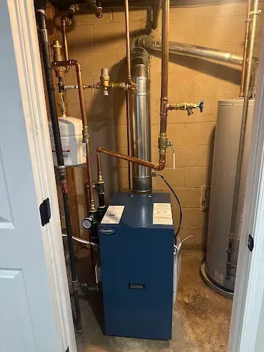 A blue furnace with copper pipes, a silver chimney, and a water heater in a closet.