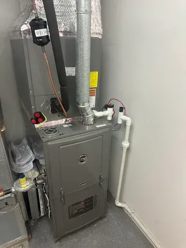 Gray furnace in a utility room with white piping and a silver exhaust pipe.