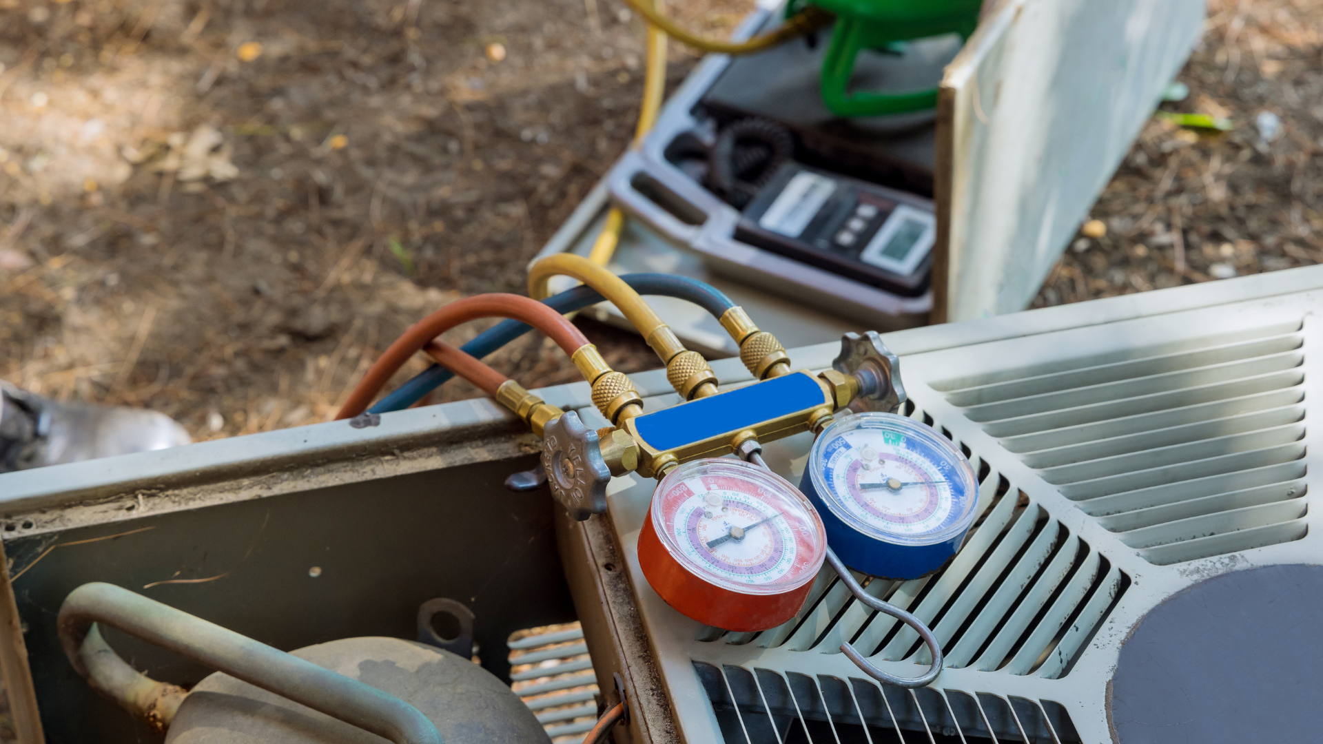 An HVAC technician gauges an air conditioner unit with hoses and gauges.