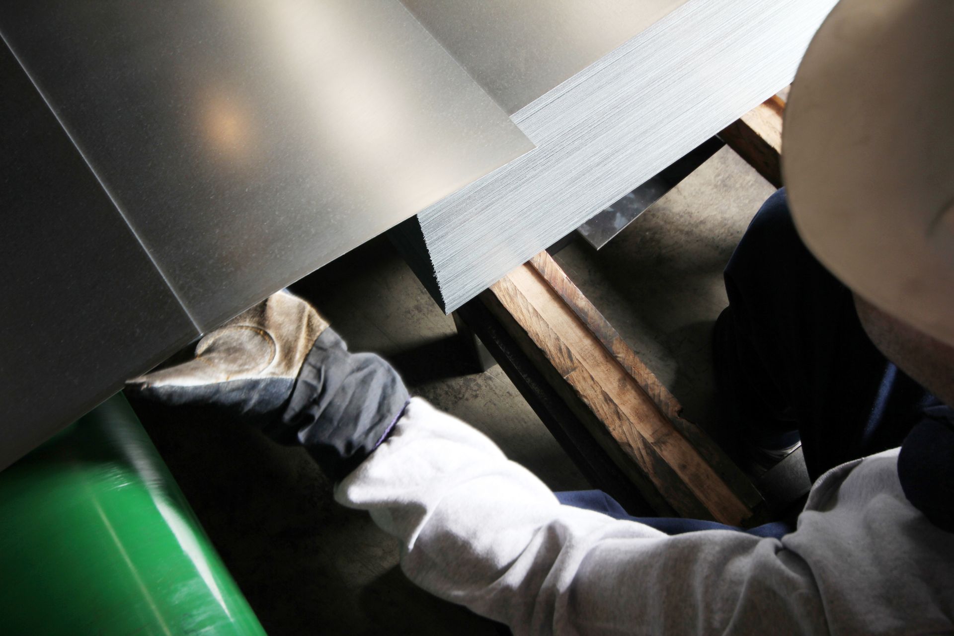 Person wearing a hard hat and gloves works with sheet metal.