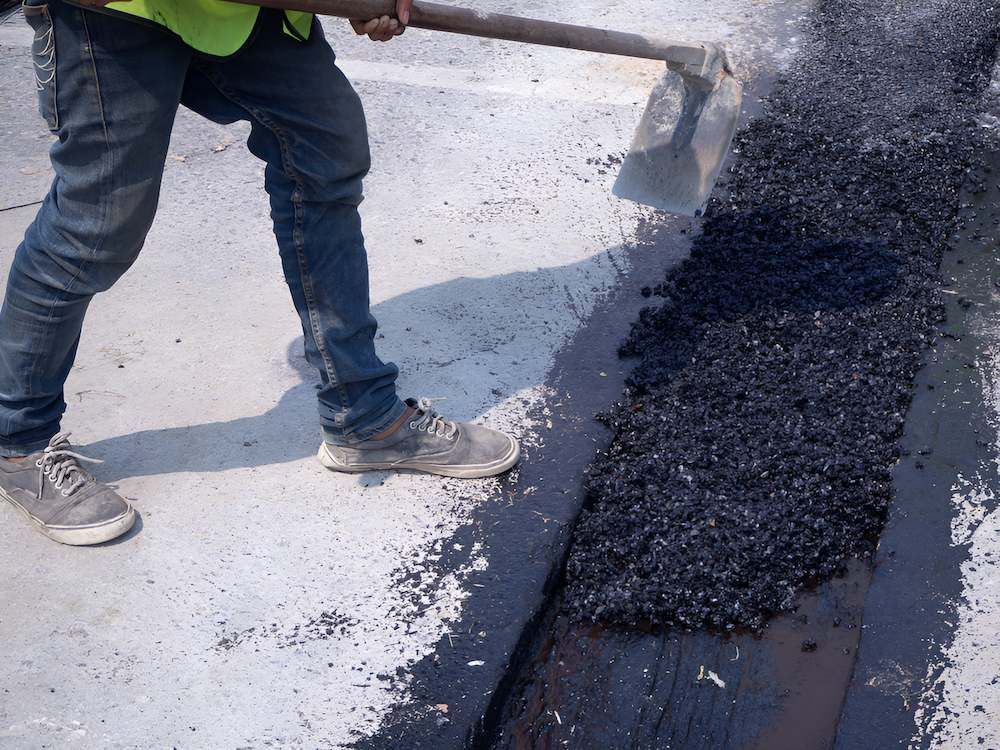 A Man is Using a Shovel to Spread Asphalt on the Ground — F & J Bitumen Services in Adelaide River, NT