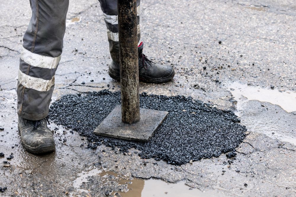 A Man is Putting Asphalt on a Hole in the Road — F & J Bitumen Services in Adelaide River, NT