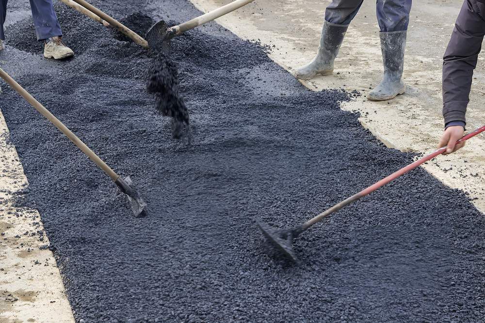 A Group of People Are Working on a Road With Shovels and Rakes — F & J Bitumen Services in Palmerston, NT