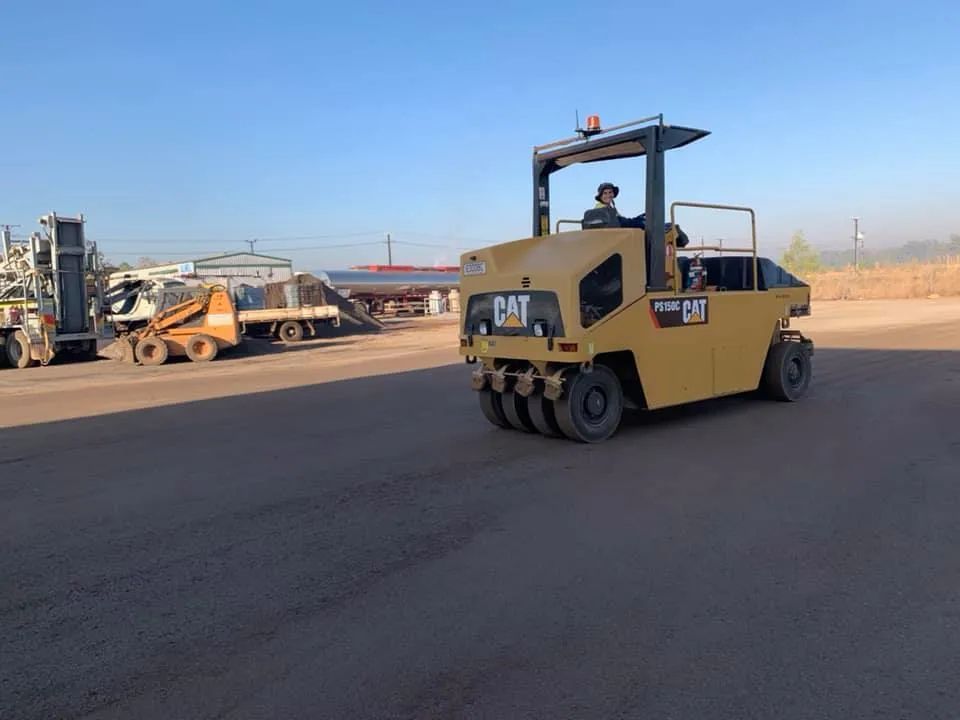 A Man is Driving a Cat Road Roller on a Dirt Road — F & J Bitumen Services in Humpty Doo, NT