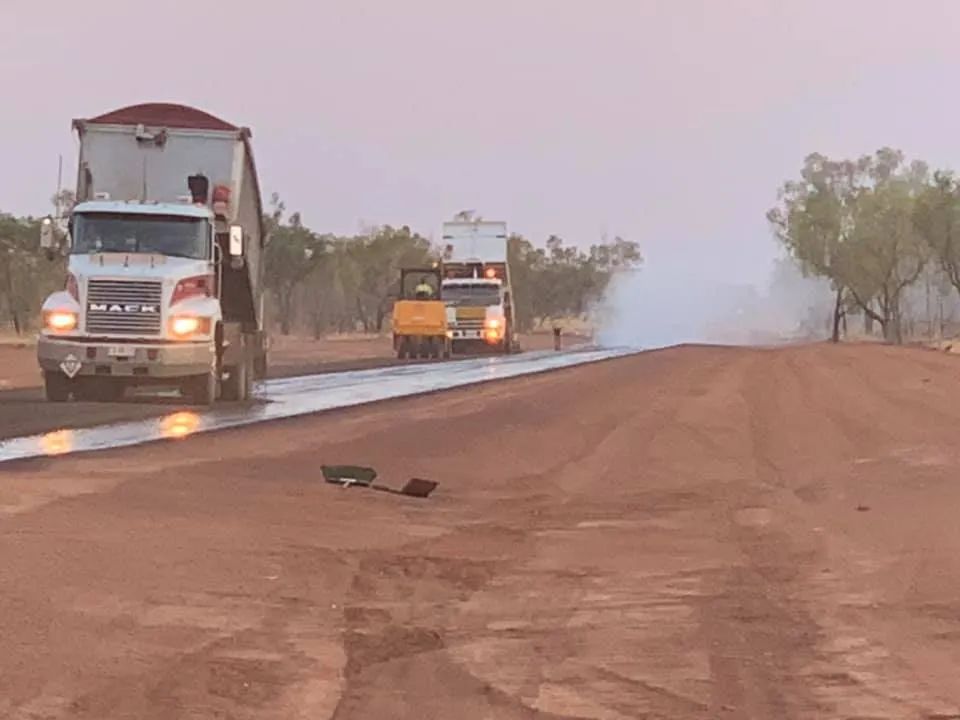 Two Mack Trucks Are Driving Down a Dirt Road — F & J Bitumen Services in Humpty Doo, NT