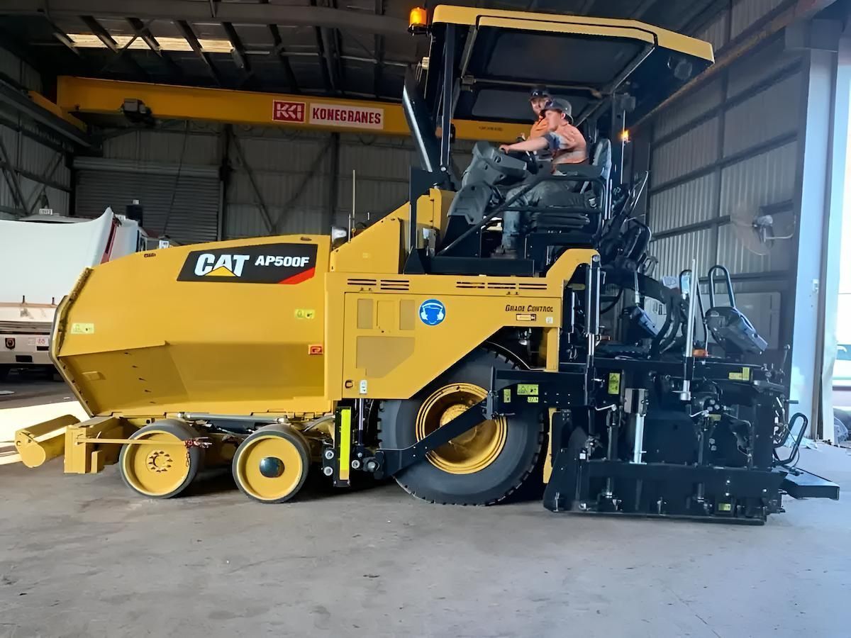 A Man is Driving a Cat Asphalt Paving Machine in a Garage — F & J Bitumen Services in Humpty Doo, NT