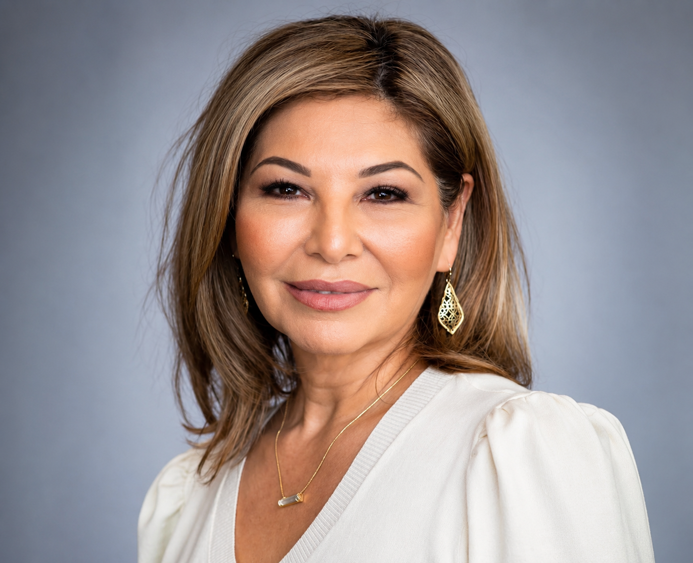 Studio headshot of a smiling person in a white blouse against a gray background