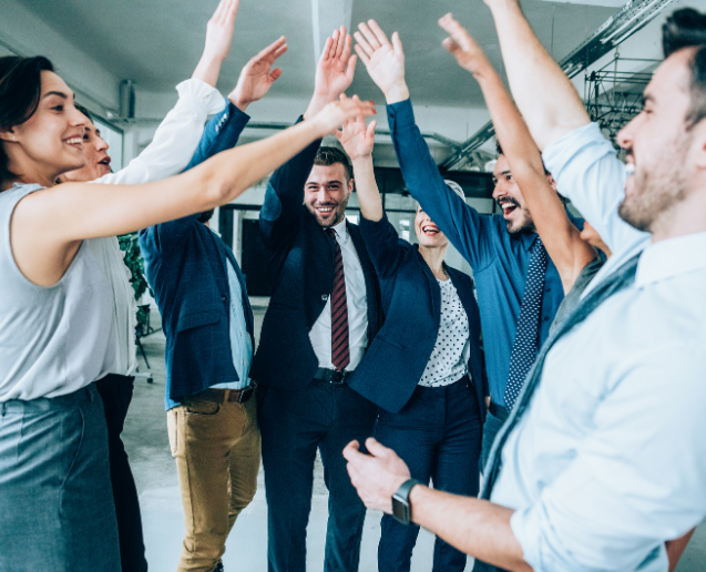 Team members in a modern office high-five in a circle, smiling and celebrating together.