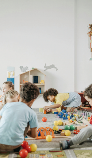Children sitting on the floor, playing with colorful toys in a bright classroom.