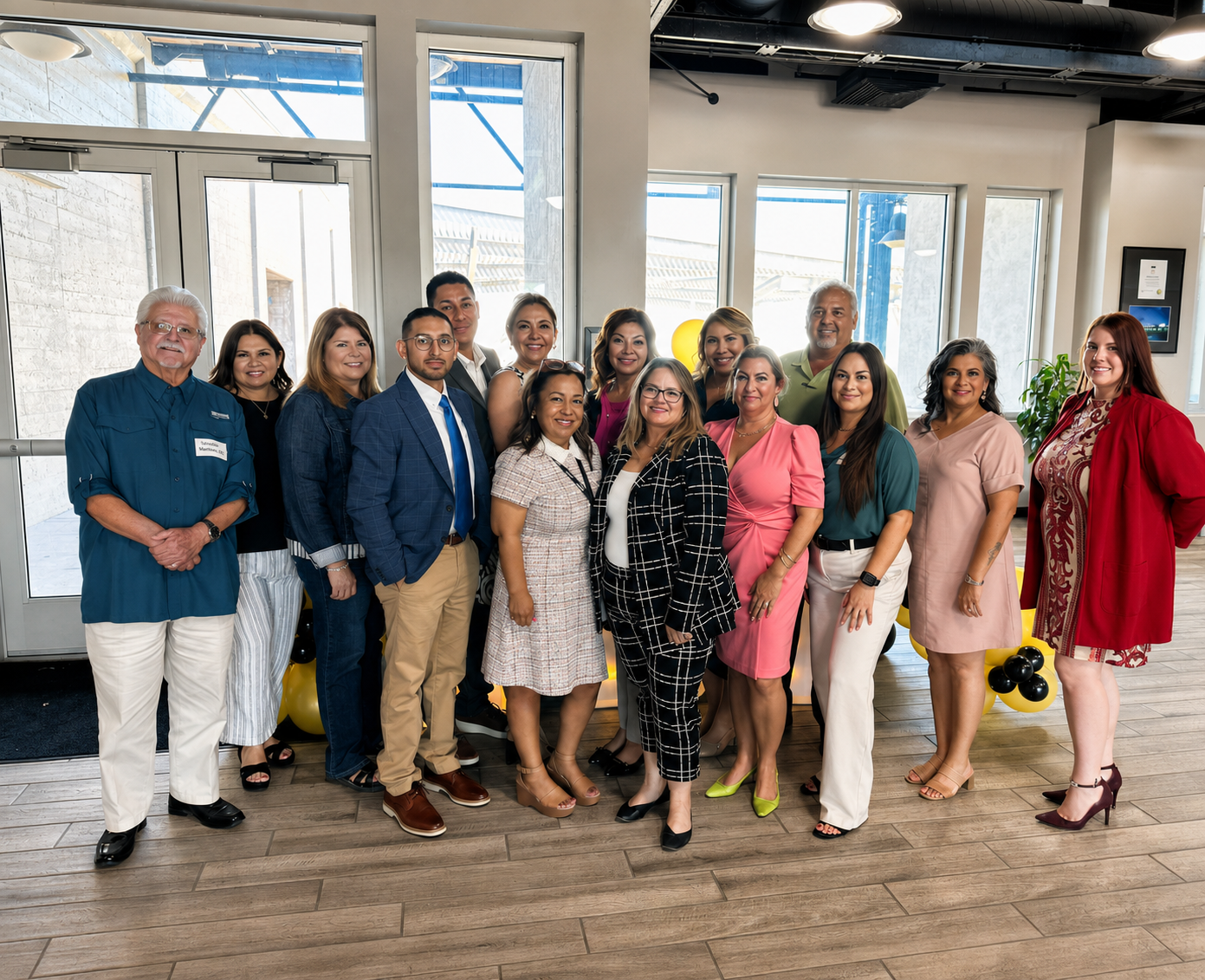 Group of people posing indoors in a bright room with large windows, wearing formal and colorful outfits.