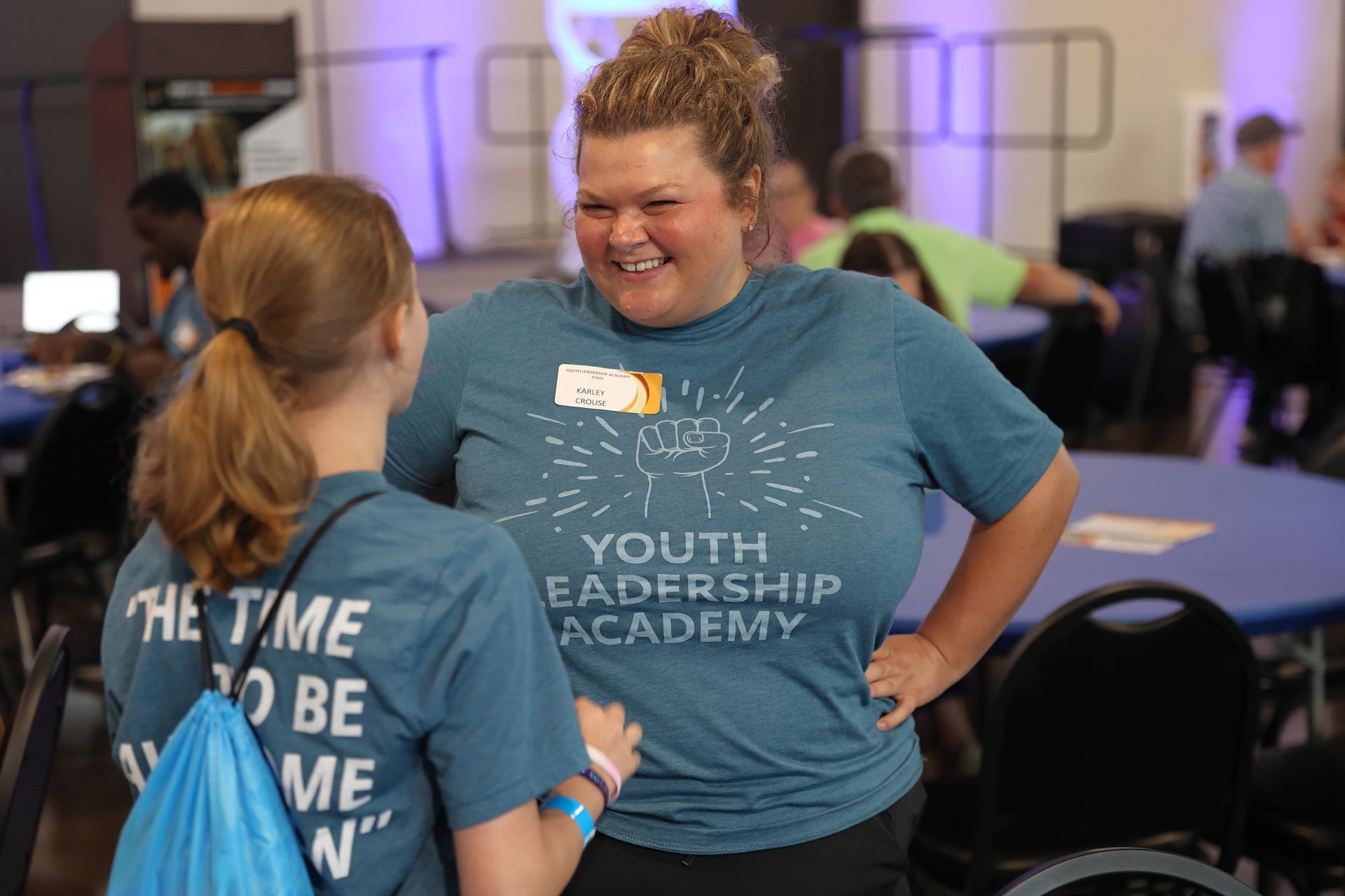 Two YLA graduates talking to each other. One is facing away from the camera. The other, whose face is visible, is smiling.