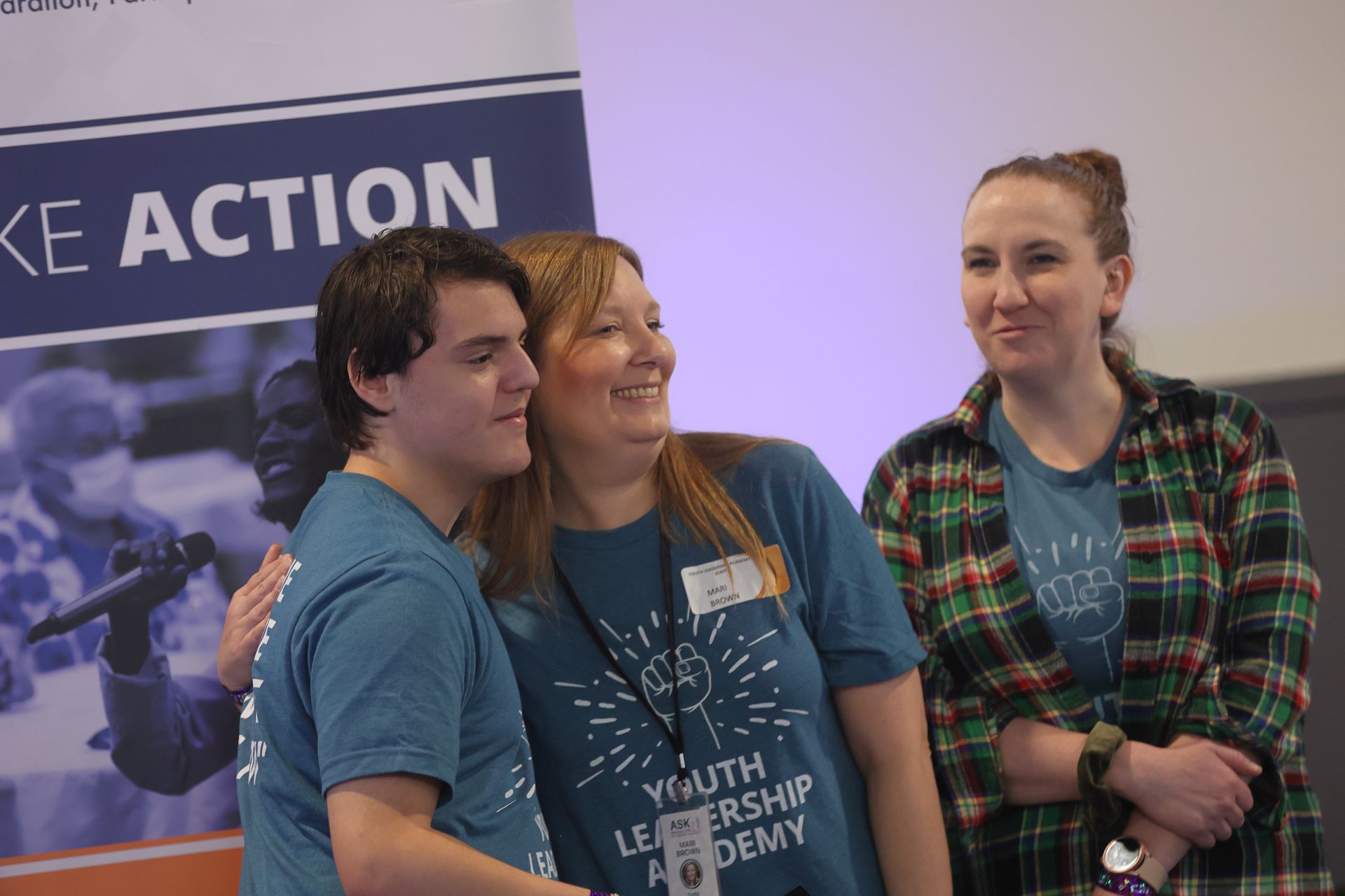 Two YLA participants hugging, while a third person stands next to them smiling.