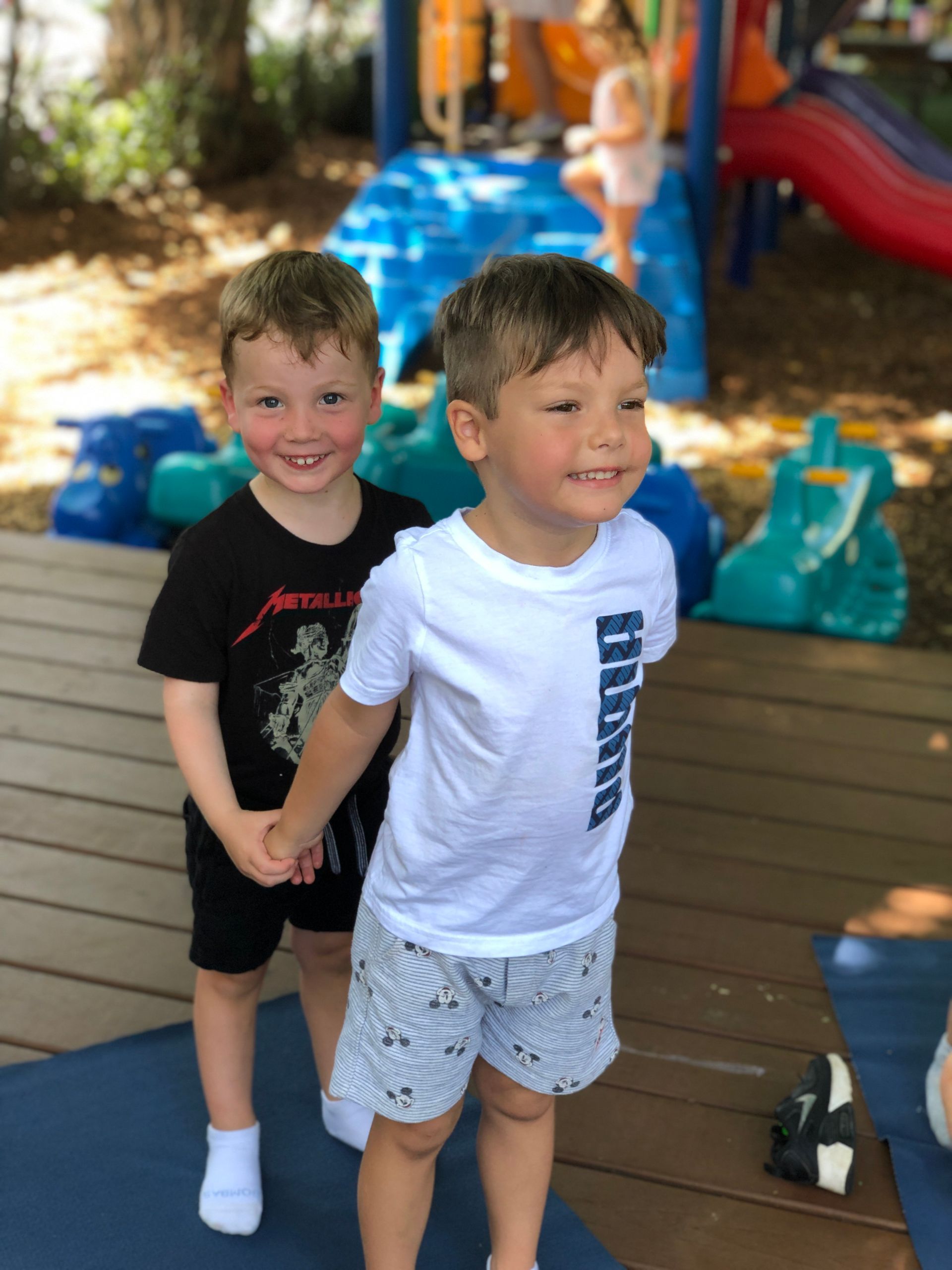 Two Montessori children standing on a wooden deck near a colorful backyard playset