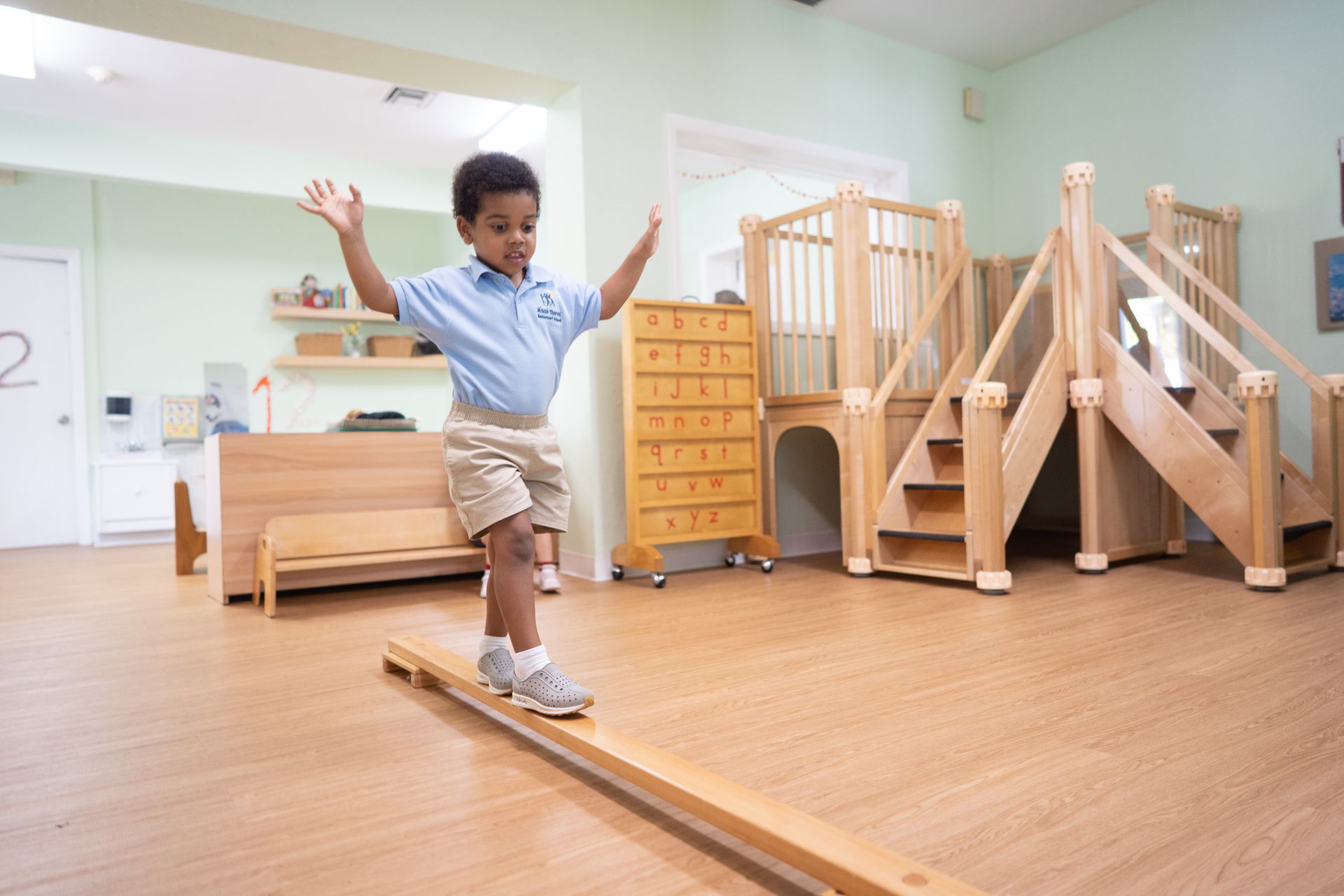 A Montessori child is balancing on a wooden balance beam in a room.