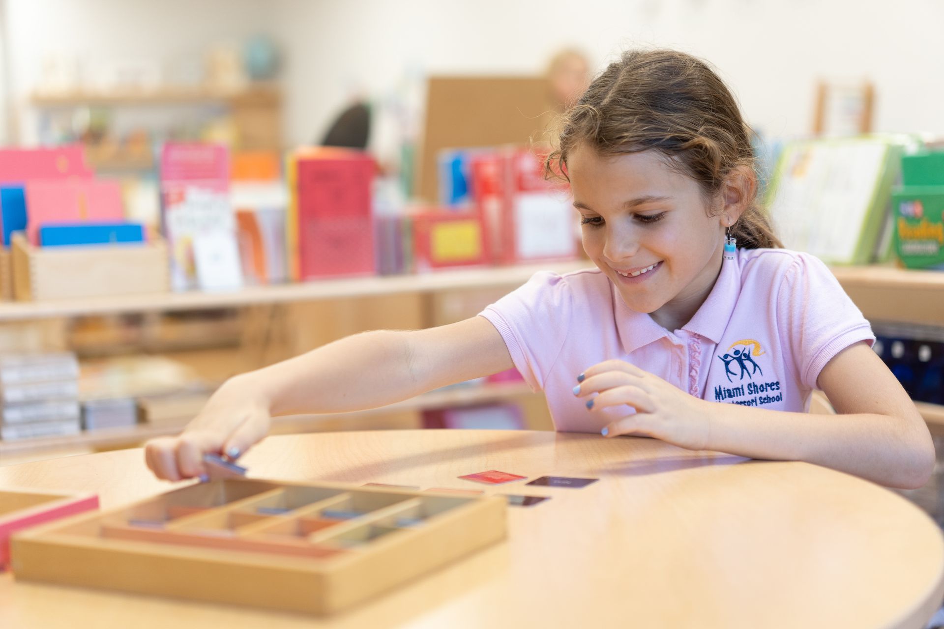 A Montessori elementary child is sitting at a table in a classroom working with materials