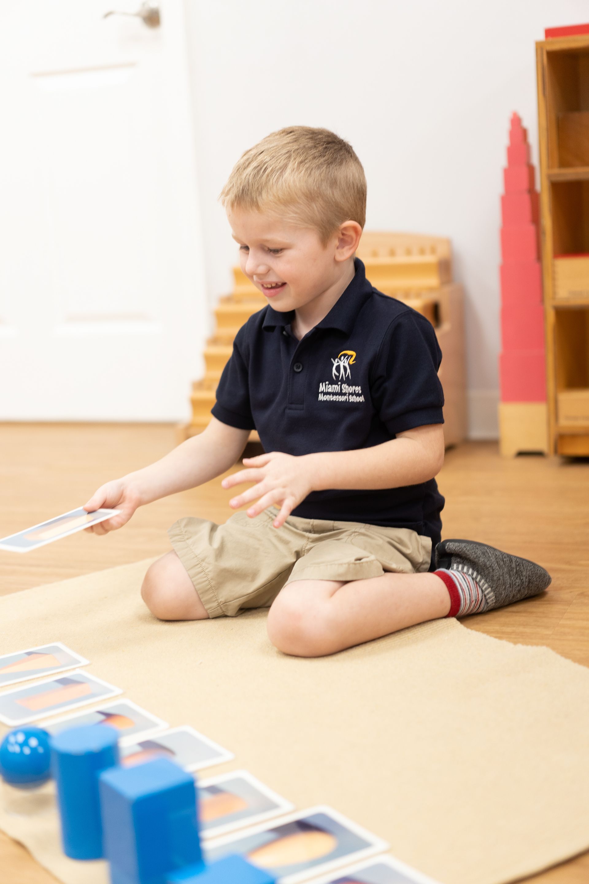 Child is sitting on the floor working with Montessori geometric volumes.