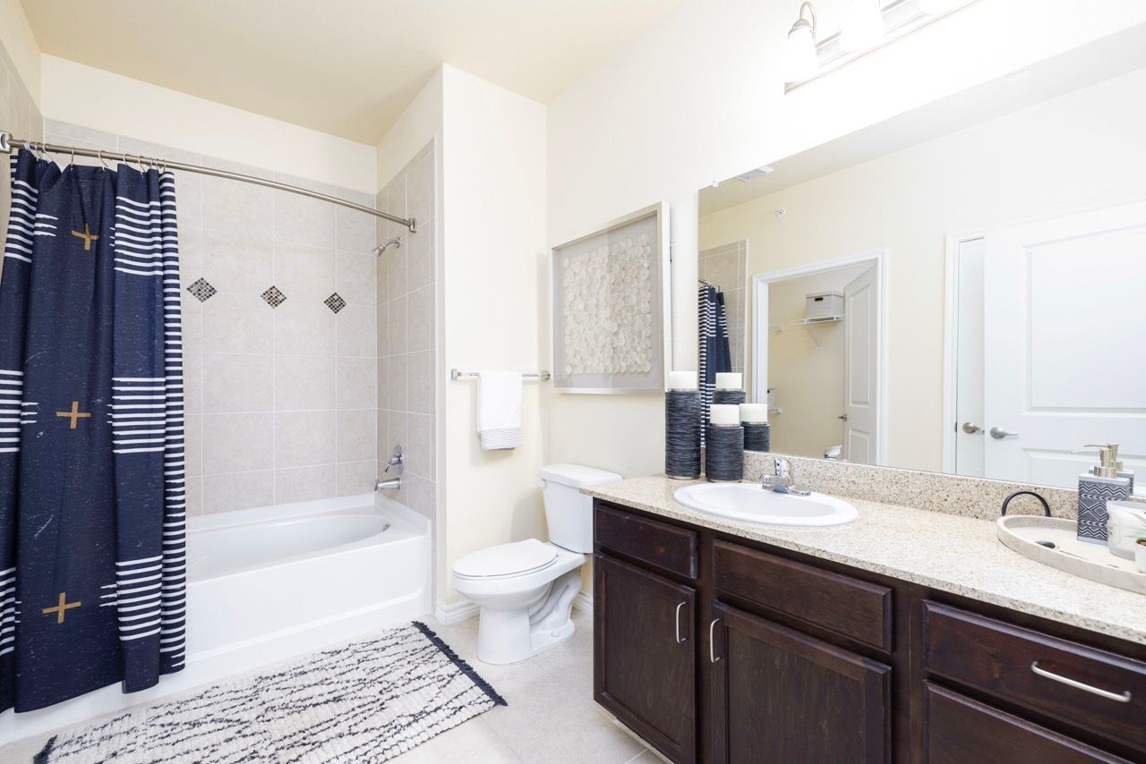 Bathroom with a double-sink vanity, granite countertop, dark wood cabinets, and a tub/shower.