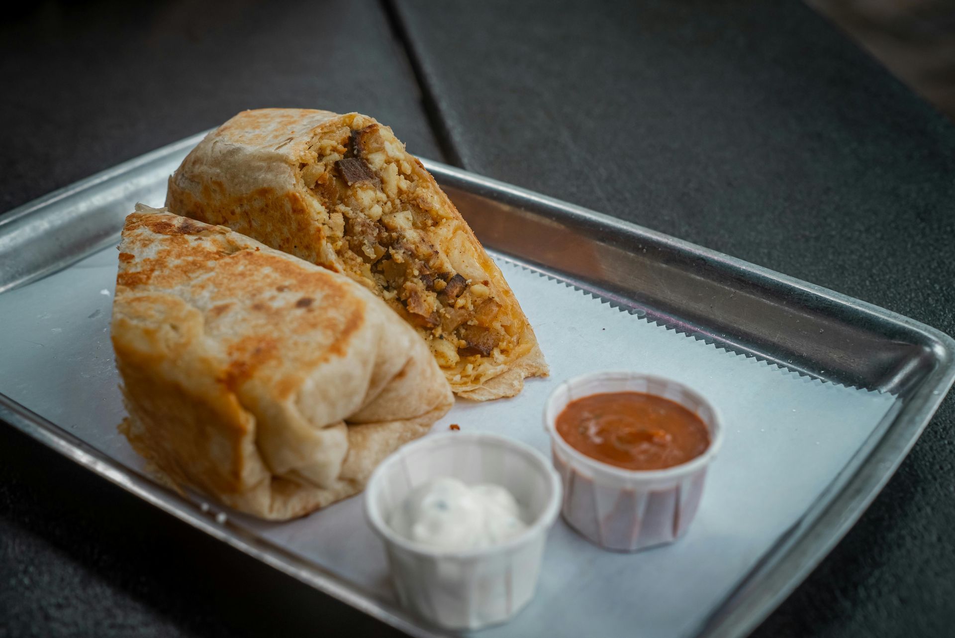 Burrito cut open on tray, served with small cups of red sauce and white dip.