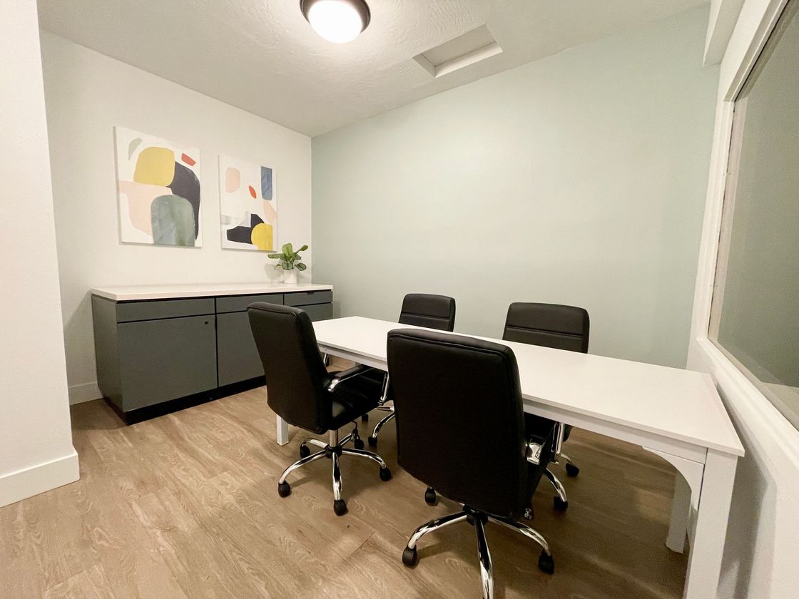 Modern conference room with white table, black chairs, gray sideboard, and abstract wall art.