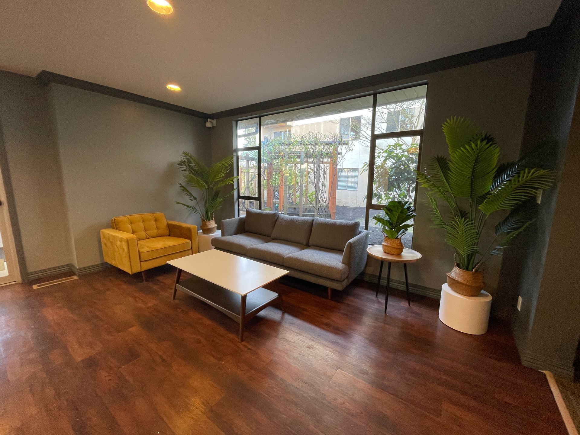 Modern living room with gray sofa, yellow chair, coffee table, and large windowed wall