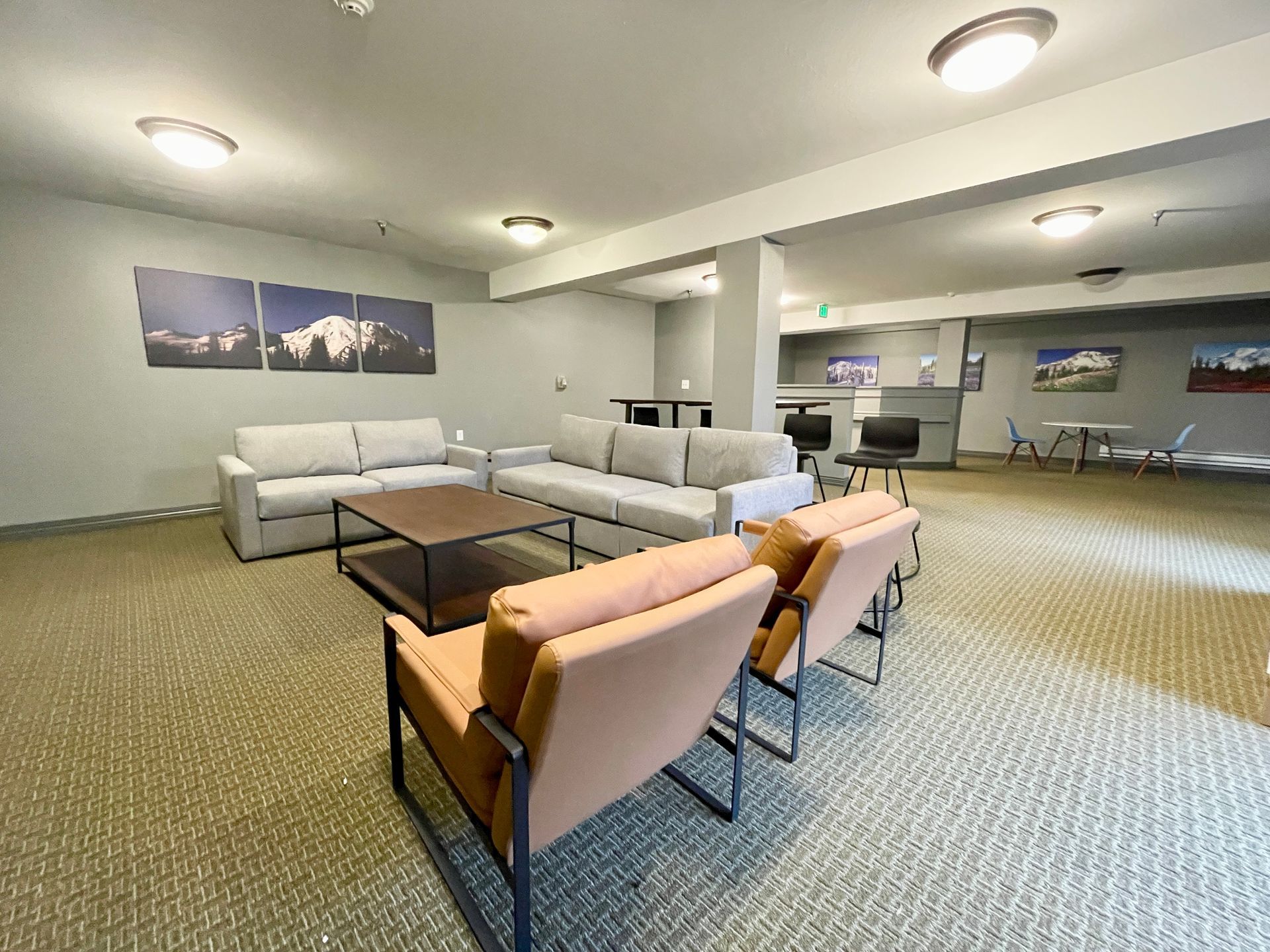 Spacious modern lounge with white sofas, tan chairs, coffee tables, and wall art under recessed ceiling lights