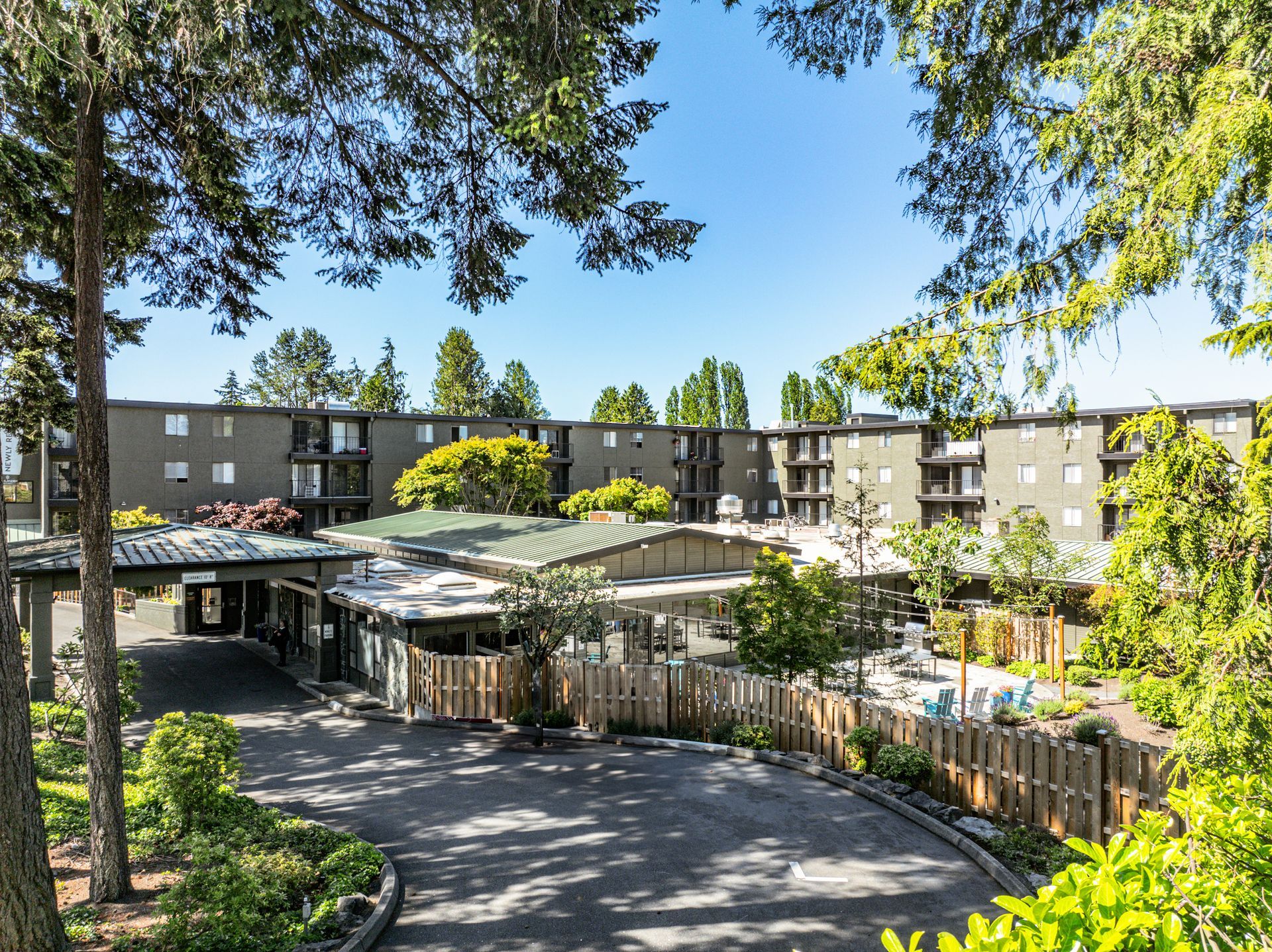 Apartment courtyard with a fenced playground and green trees under a clear blue sky