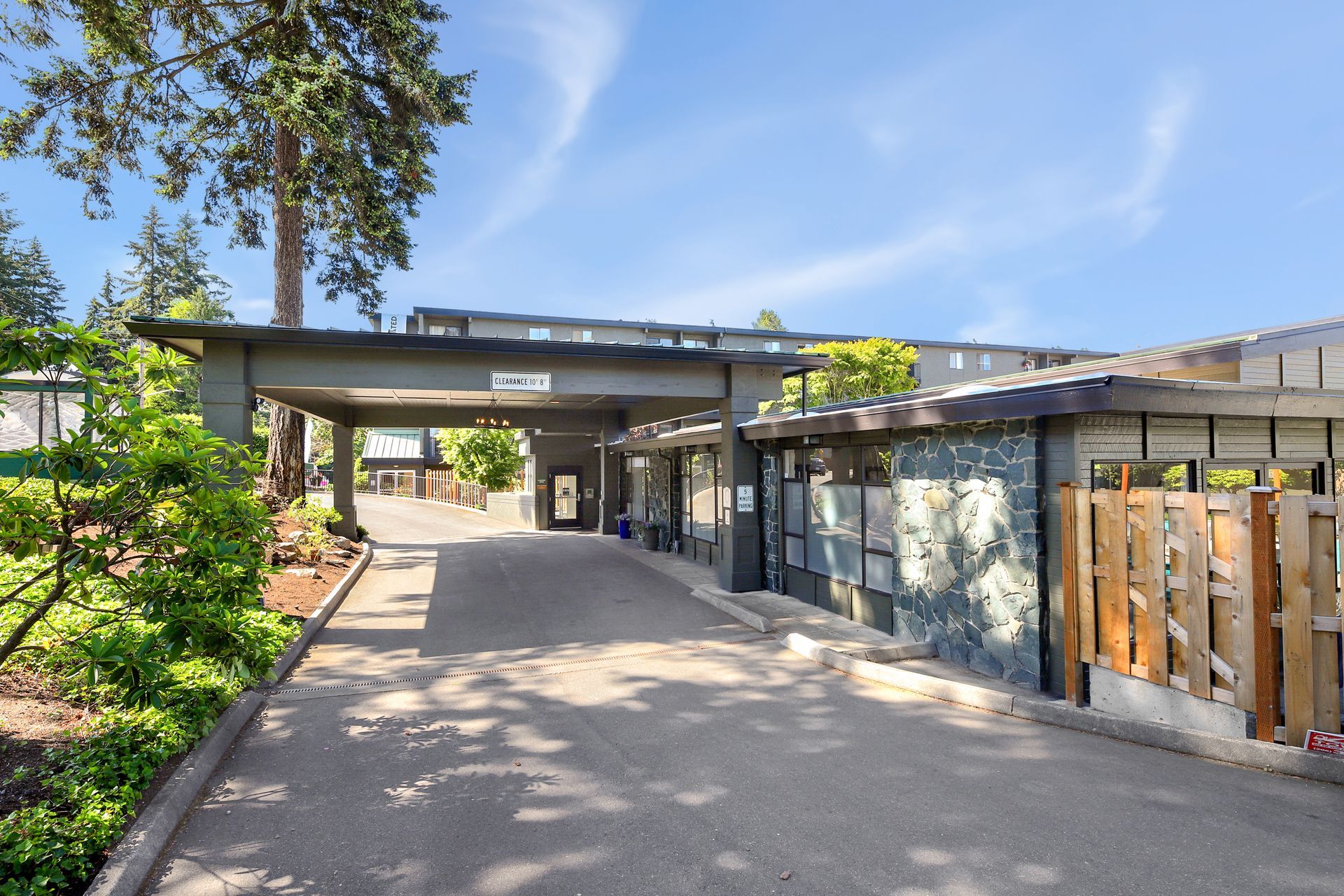 Modern building entrance with a covered walkway, trees, and a wooden fence on the right