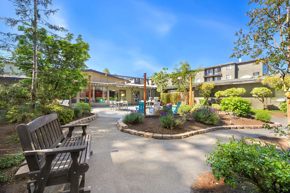 Courtyard garden with benches, flowers, and a fountain outside a building under a blue sky