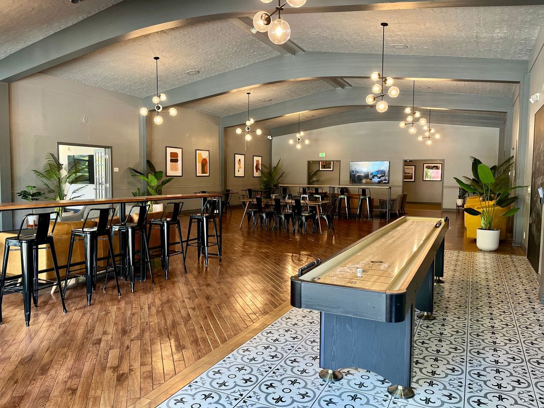Spacious modern café with wooden floors, bar seating, hanging lights, and long communal tables