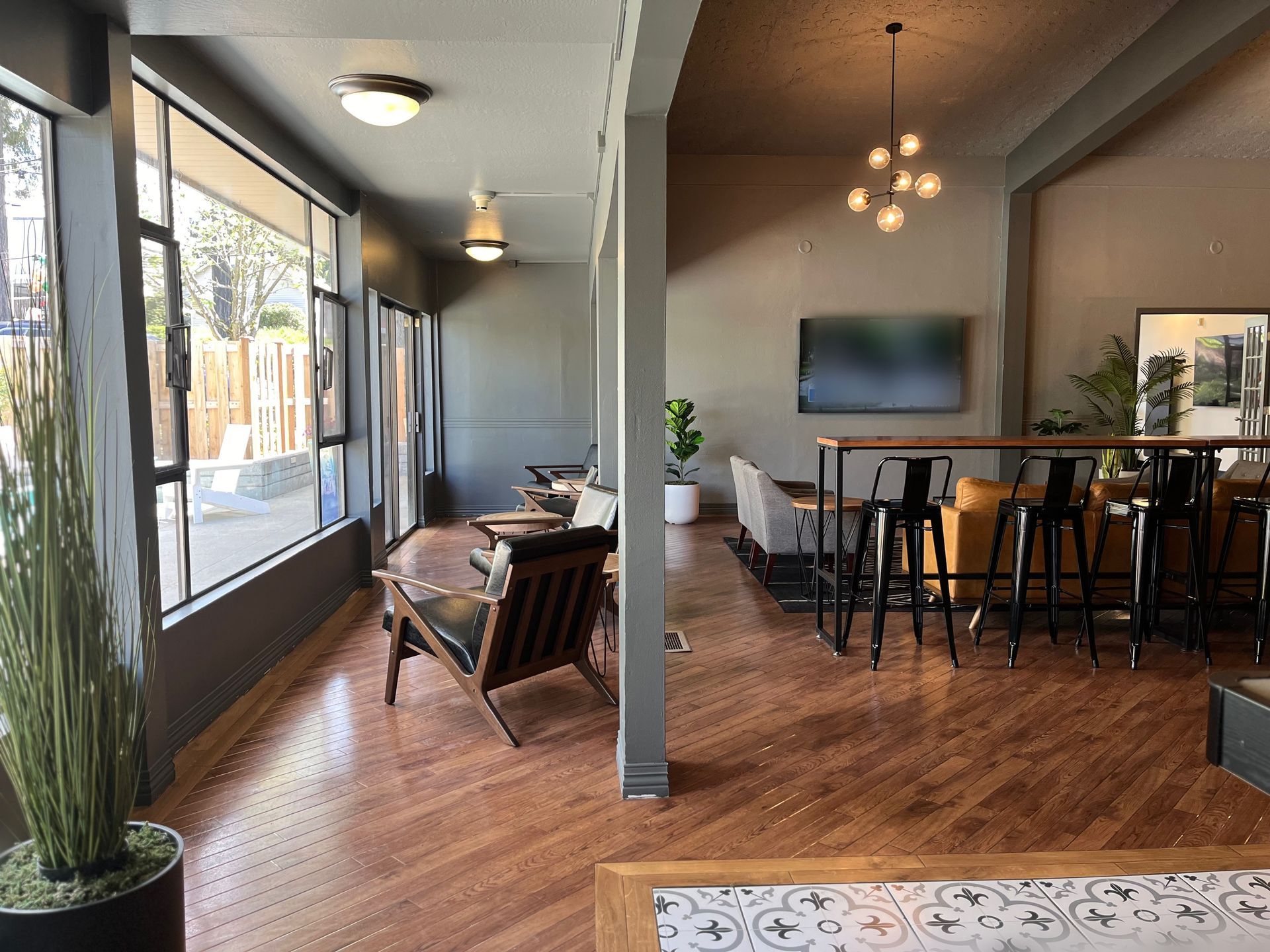 Modern living room with wood floors, large windows, sofa, chairs, and a dining table under pendant lights