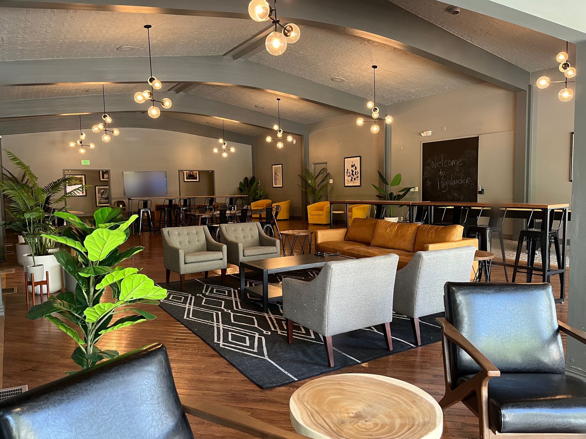 Cozy modern lounge with sofas, chairs, pendant lights, and a blackboard in a spacious room
