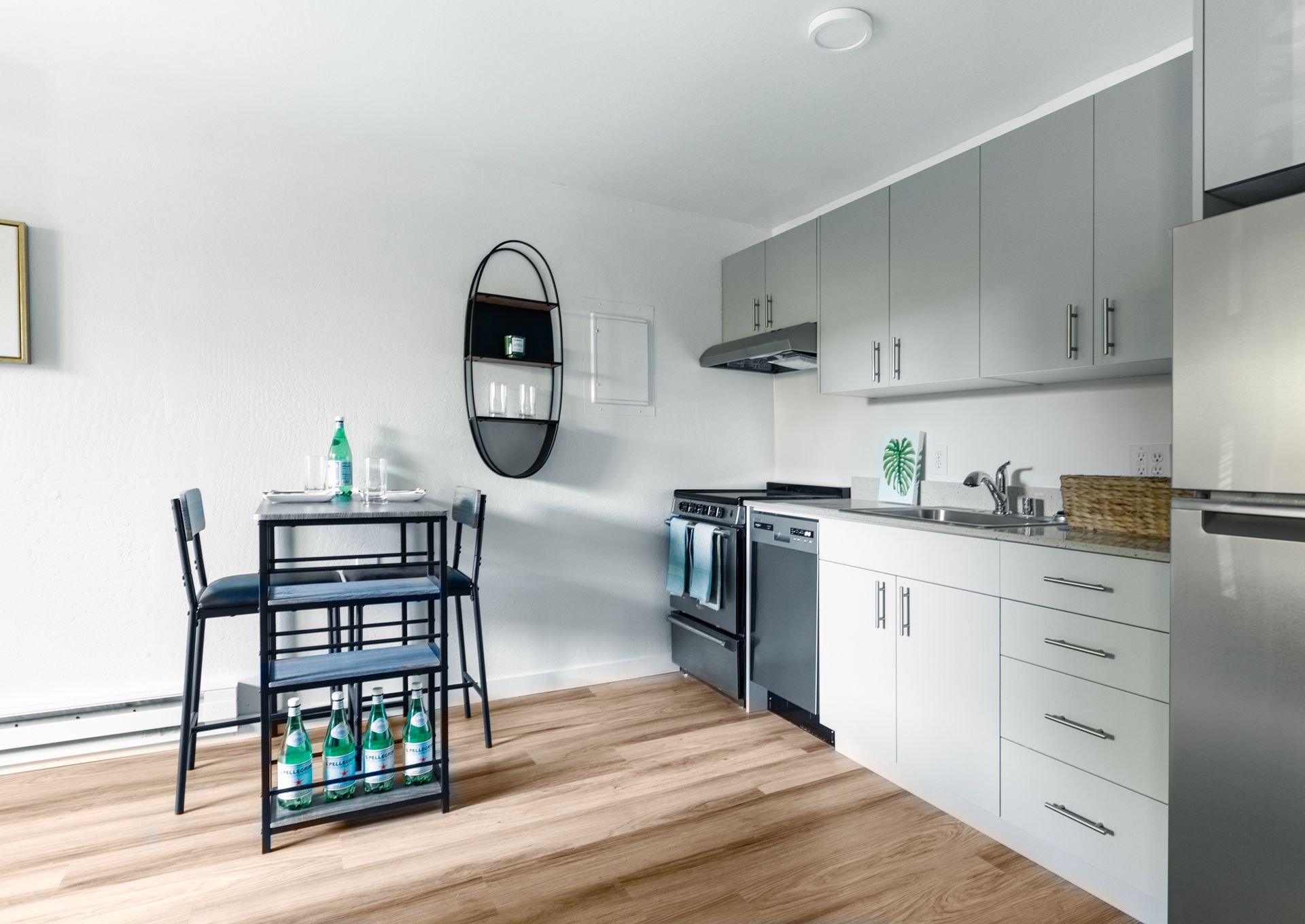 Bright white kitchen with gray cabinets, a small black dining table, and wood flooring